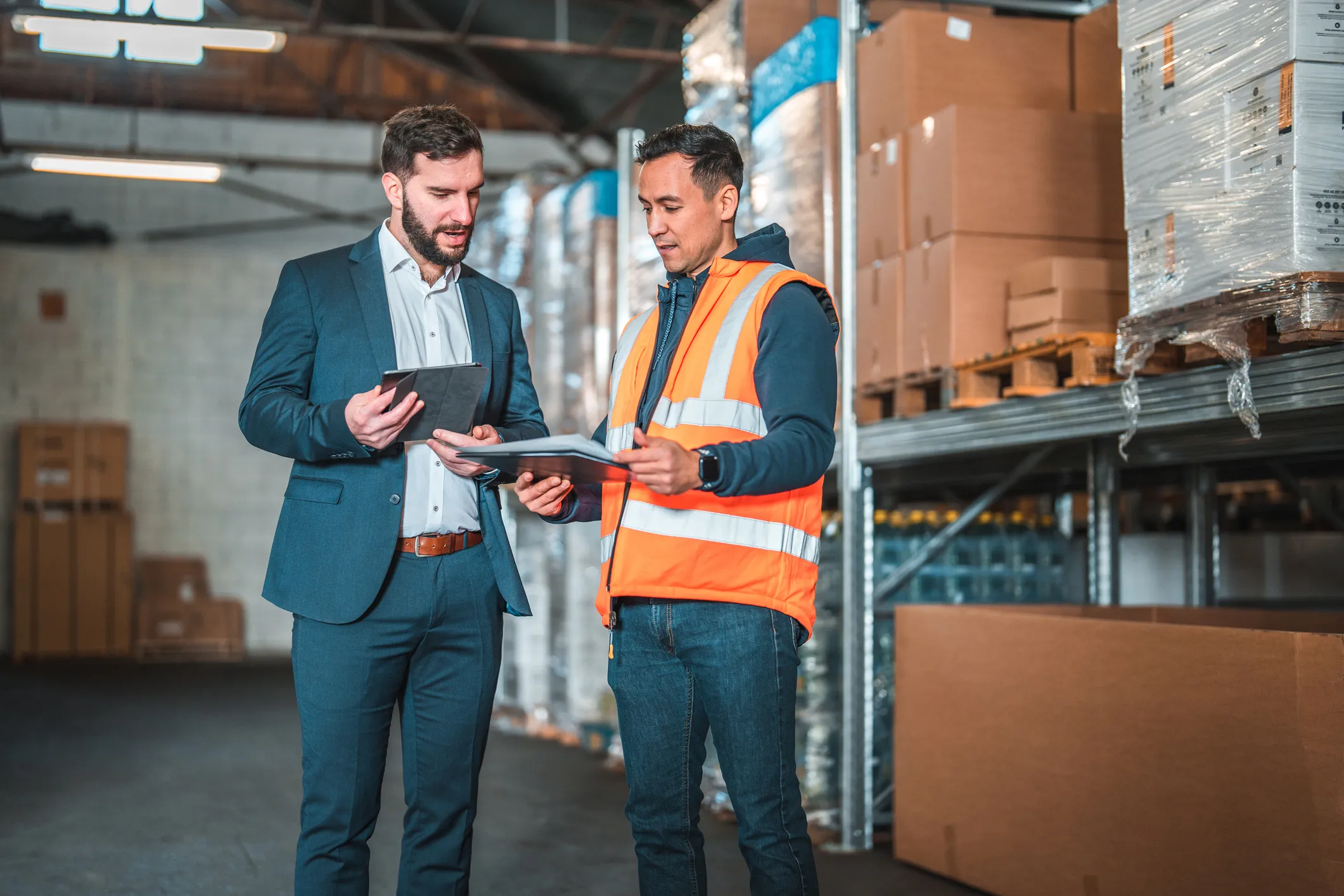 Three professionals reviewing operations on a tablet and handheld scanner in a warehouse